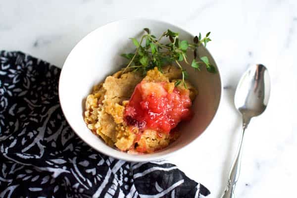 Bowl of strawberry dump cake on a marble table with fabric and spoon next to it. 