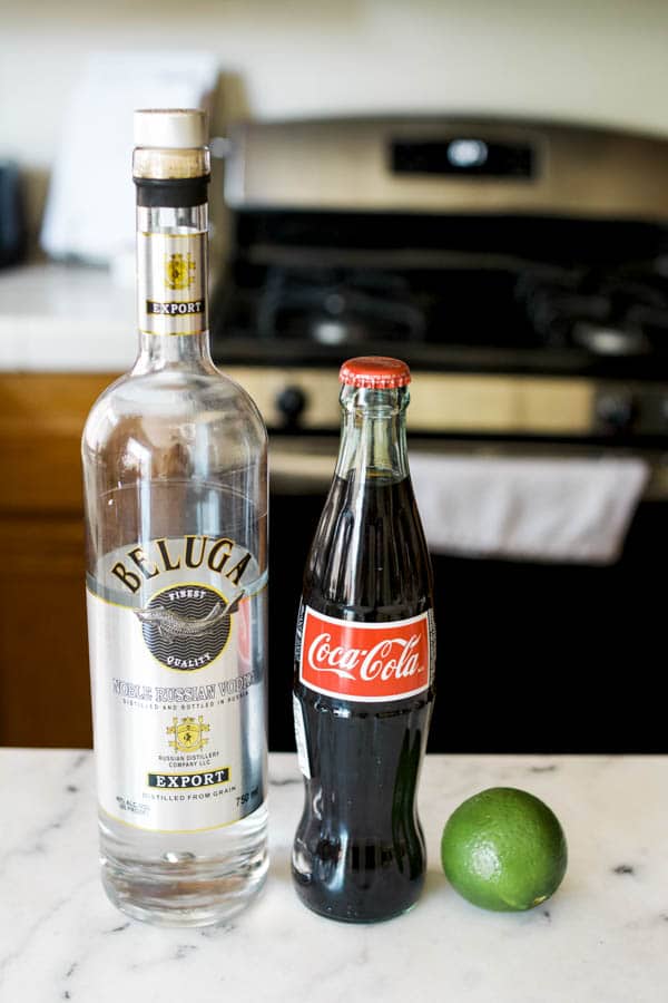 Bottle of vodka and coke on a cutting board with a lime.