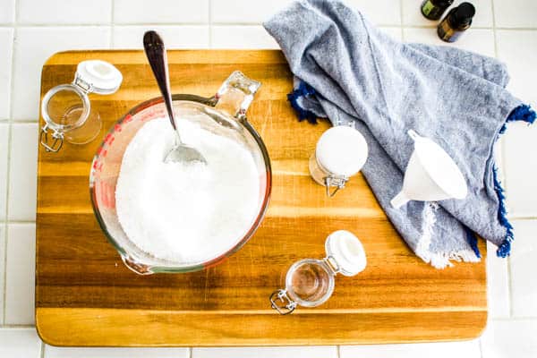 A glass measuring cup of diy bath salts and empty glass jars and a funnel to put them in. 