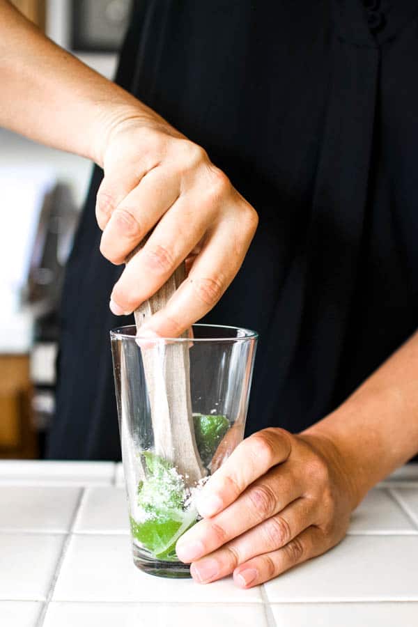 Woman muddling sugar, mint and lime for a mojito cocktail.