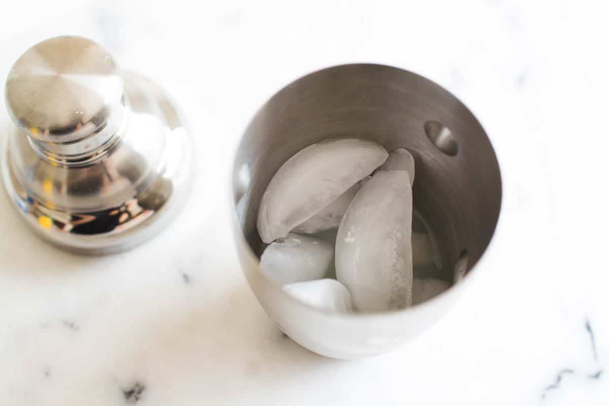 An overhead view of ice in a cocktail shaker on a marble cutting board.