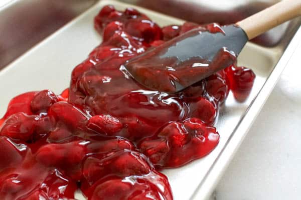 Strawberry pie filling being spread into a cake pan for a dump cake.