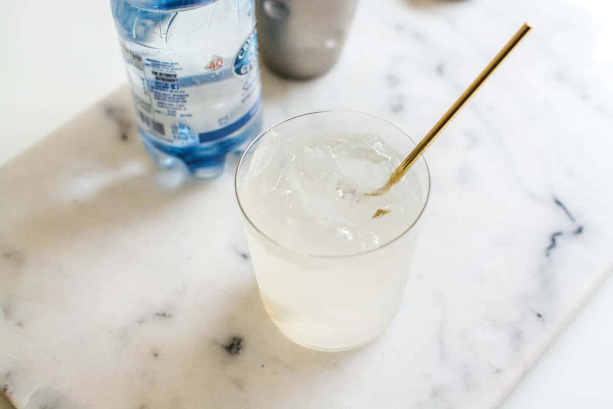 Overhead shot of a tequila cocktail on a marble cutting board with a gold bar spoon.