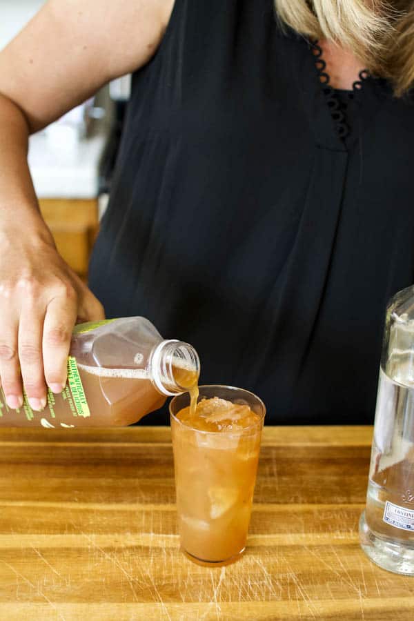 Girl adding apple juice to a glass with ice and vodka for an easy cocktail.