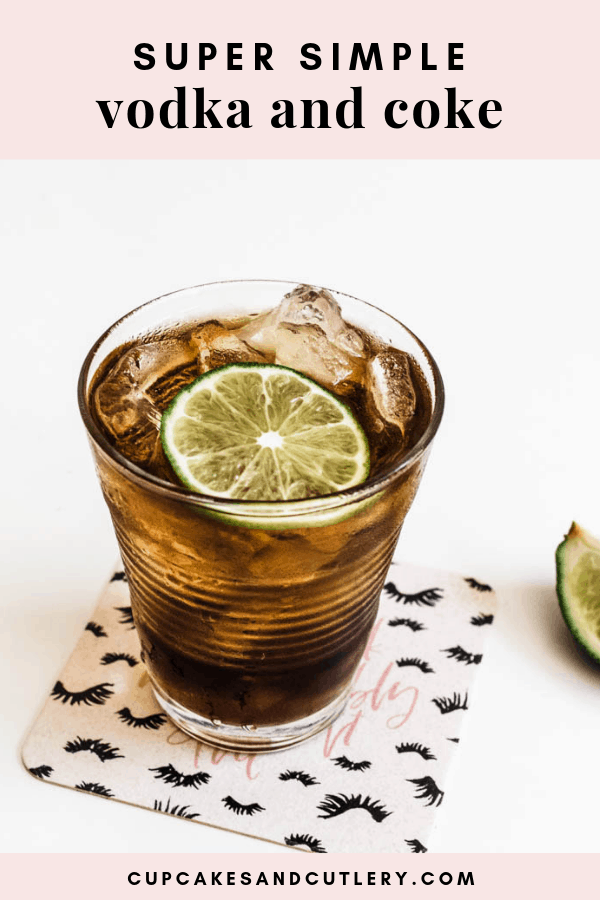 a glass of coke with ice and a lime slice on a coaster on a table.