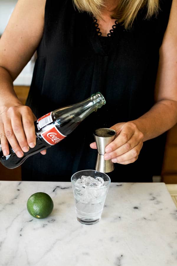 woman pouring coke into a cocktail jigger at a counter