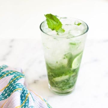 A cocktail with limes and mint on a table.