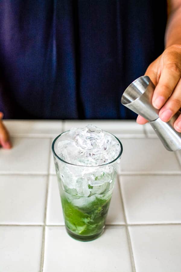 Woman adding vodka to a mojito cocktail in a tall glass. 