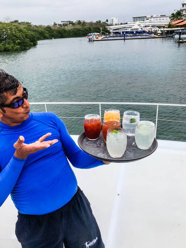 Man holding a tray of cocktails on the front of a boat.