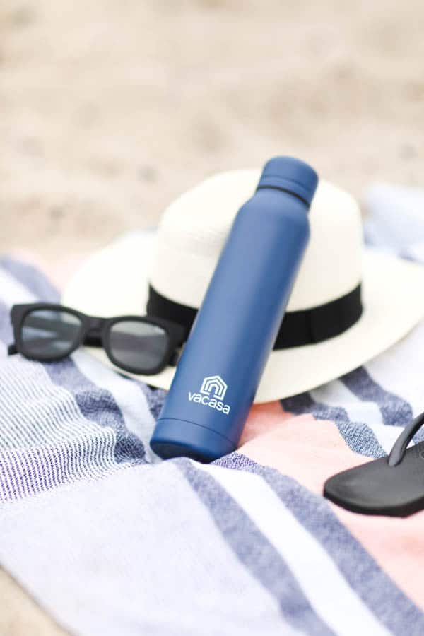 water bottle on a beach towel with hat and sunglasses.