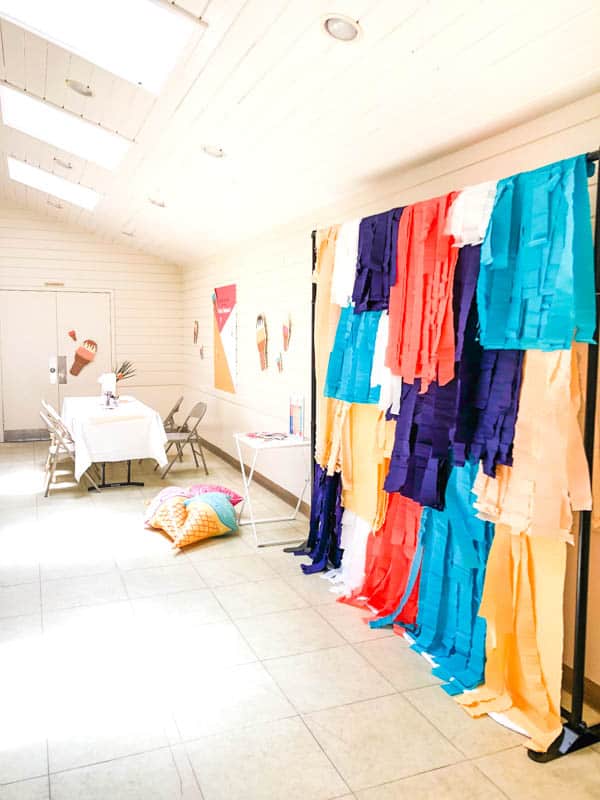 a colorful fringe photo booth backdrop and a table in a party space. 