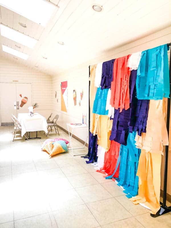 a colorful fringe photo booth backdrop and a table in a party space. 