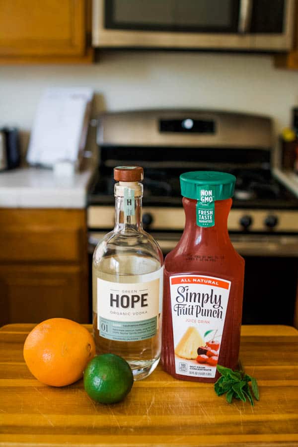 ingredients to make a fruit punch vodka cocktail on a cutting board.