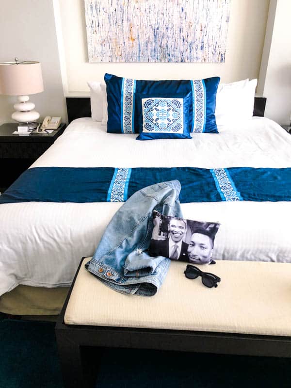 A bed in the primary room of the Marival Distinct with a jean jacket, sunglasses and a pouch on the bend at the foot of the bed.
