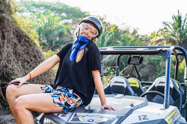 Woman sitting on top of an ATV with helmet and goggles.