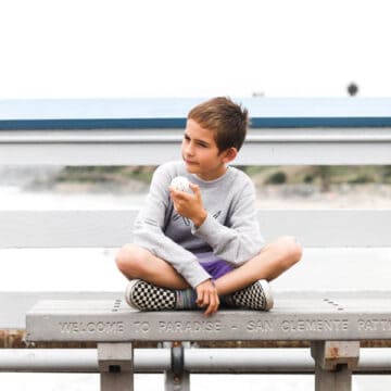 boy sitting on a bench on the san clemente pier with a jawbreaker