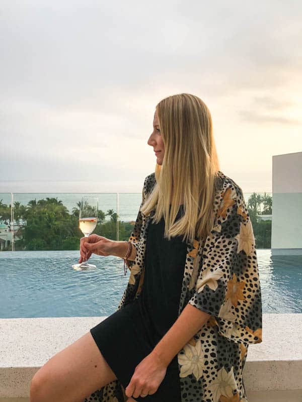 girl sitting holding a glass of champagne with the sunset behind her.