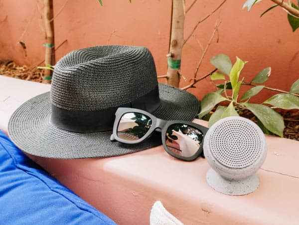 women's travel essentials including a hat, sunglasses and portable speaker on a bench