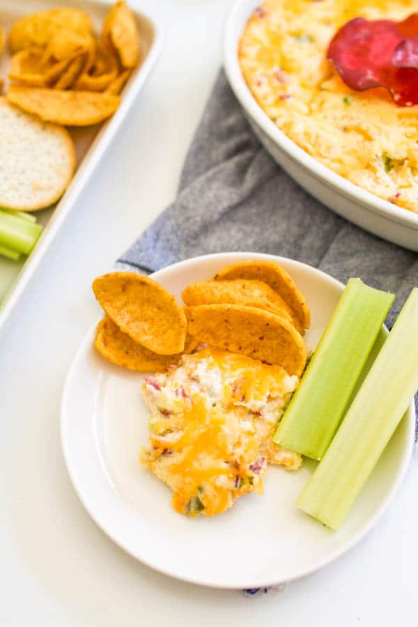 A scoop of Jalapeno Popper Dip on a small plate with chips and celery.