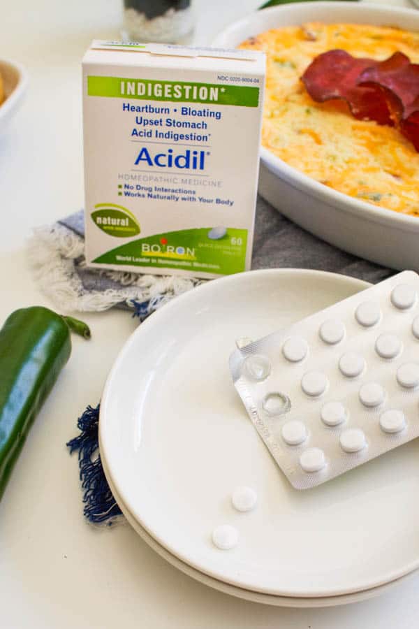 Boiron Acidil Tablets on a white plate next to a spicy dip.