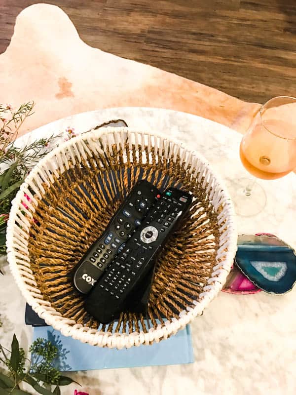 Remote controls in a basket on a table next to a glass fo rose.