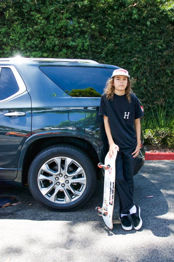 Boy standing next to wheel well of a Chevy Traverse holding a skateboard