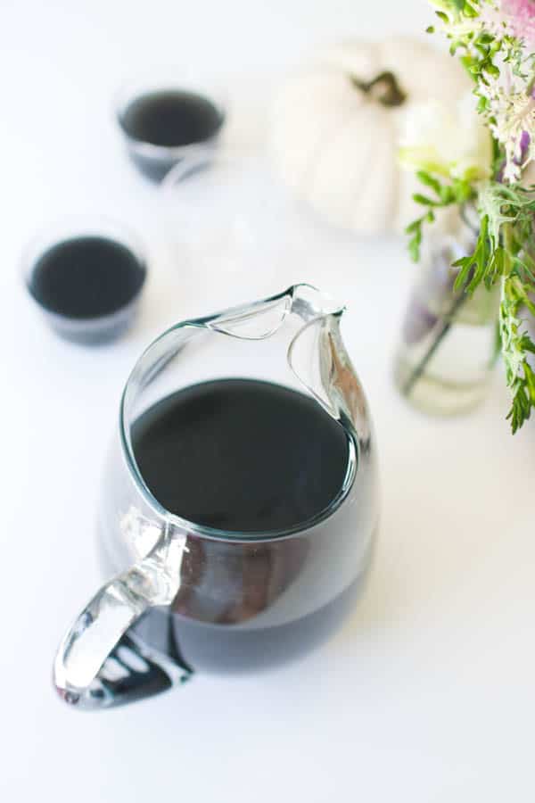 Black cocktail punch for Halloween on a table next to punch in glasses.