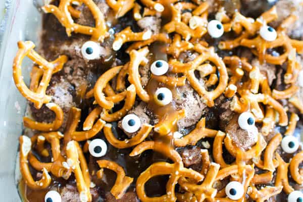Close up image of a Halloween dump cake idea with candy bars and topped with pretzels and candy eyes.