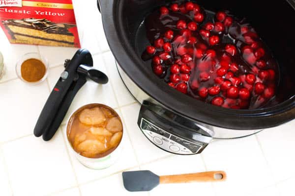 Cherry pie filling in a slow cooker next to apples.