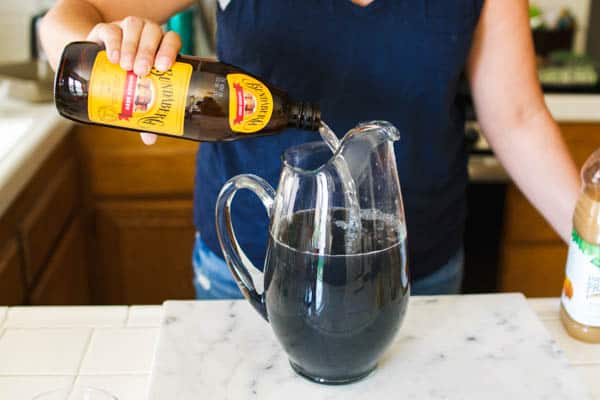 Woman pouring ginger beer in a pitcher for a Halloween vodka punch recipe.