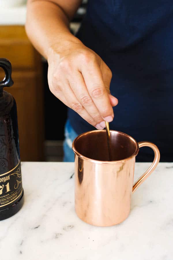 Hand stirring a Blackberry Moscow Mule in a copper mug.