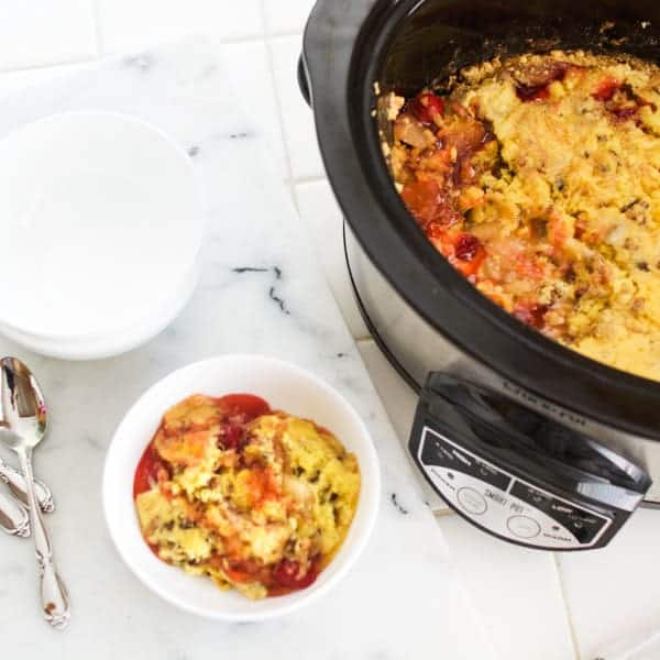 Apple cherry dump cake in a crockpot and a serving bowl on a counter.