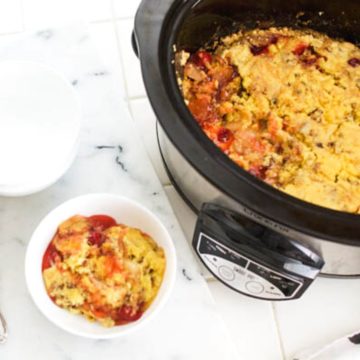 A crockpot with Apple Cherry Dump Cake in it and a portion in a dessert bowl next to it.