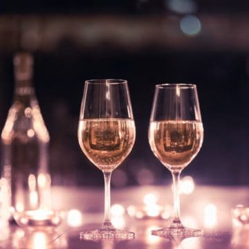 Close up of wine in wine glasses on a table covered in lights.