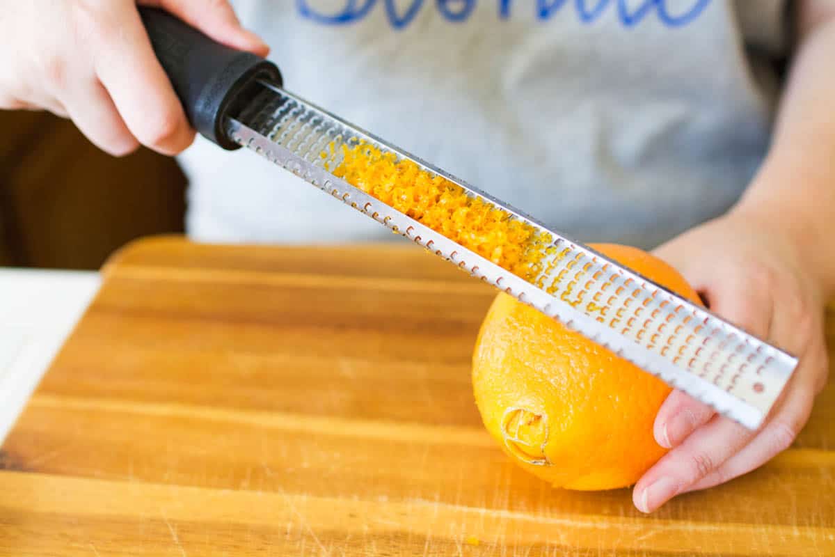 A woman zesting the peel of an orange.