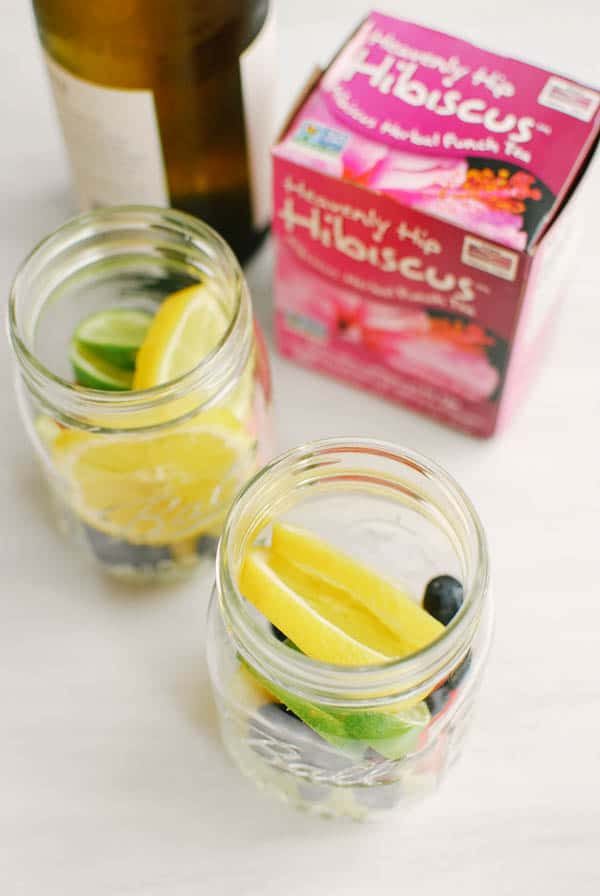 Jars with cut up fresh fruit next to a box of Hibiscus tea and a bottle of white wine.