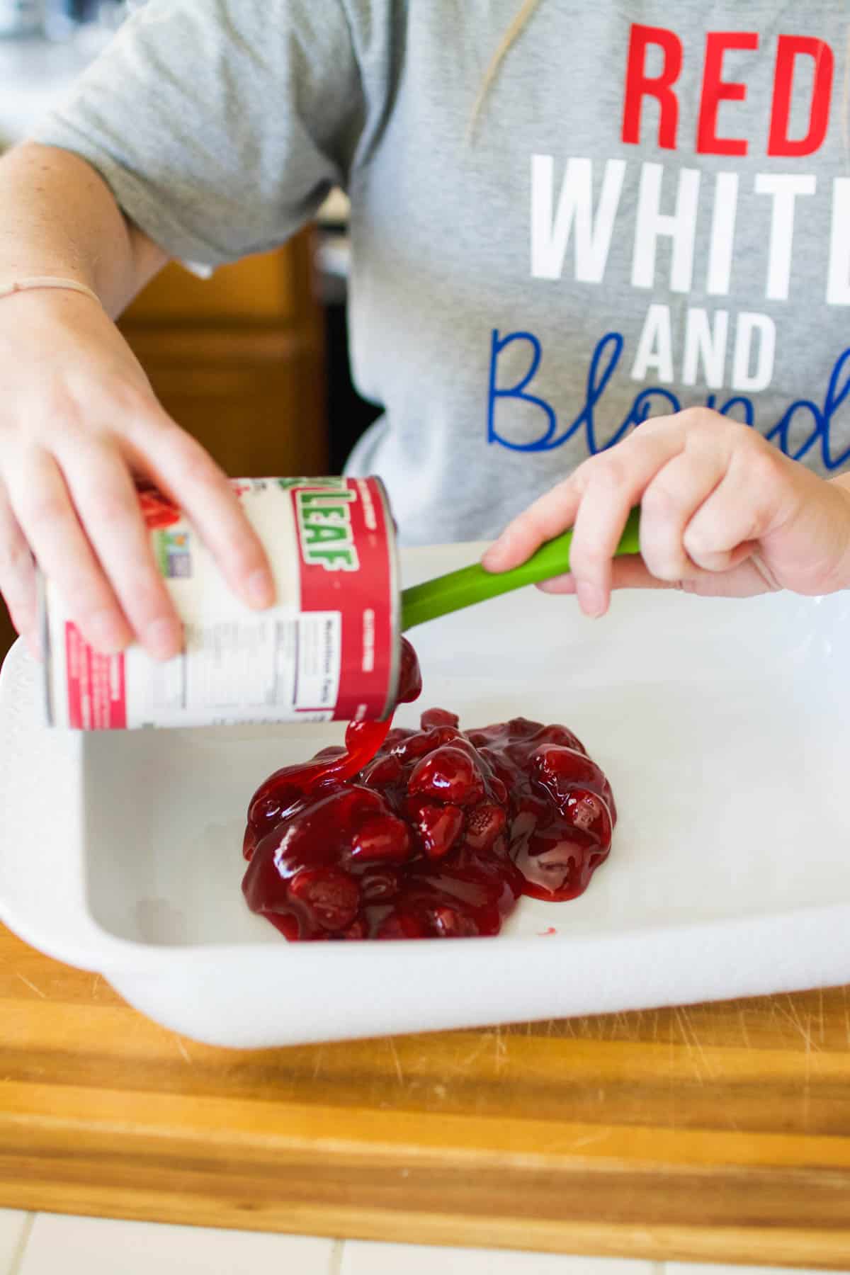 A girl using a spatula to put strawberry pie filling in a baking dish.
