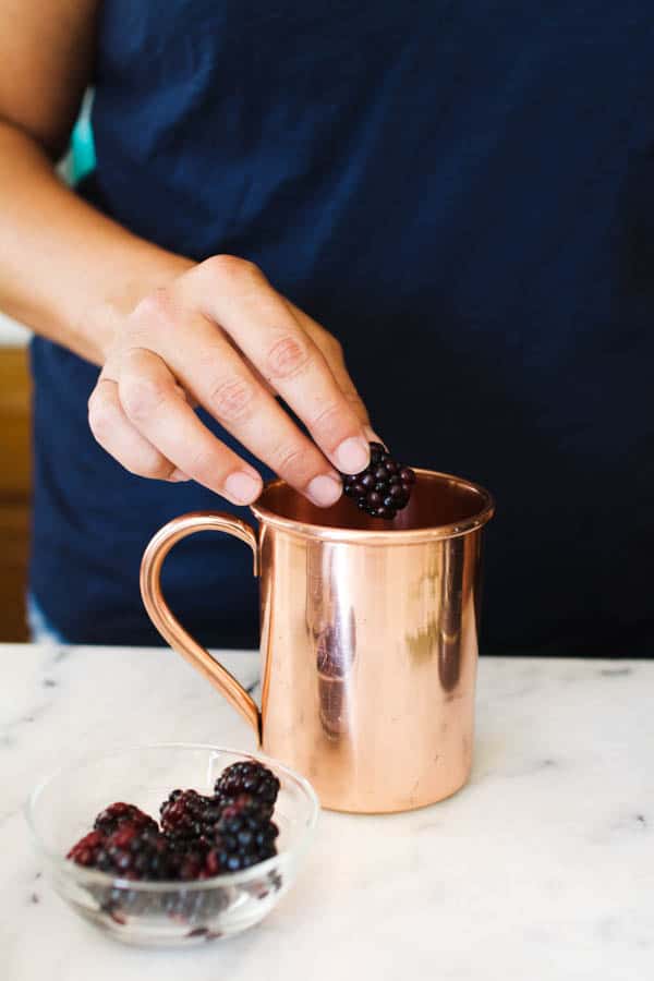 Adding blackberries to a copper Moscow Mule mug.