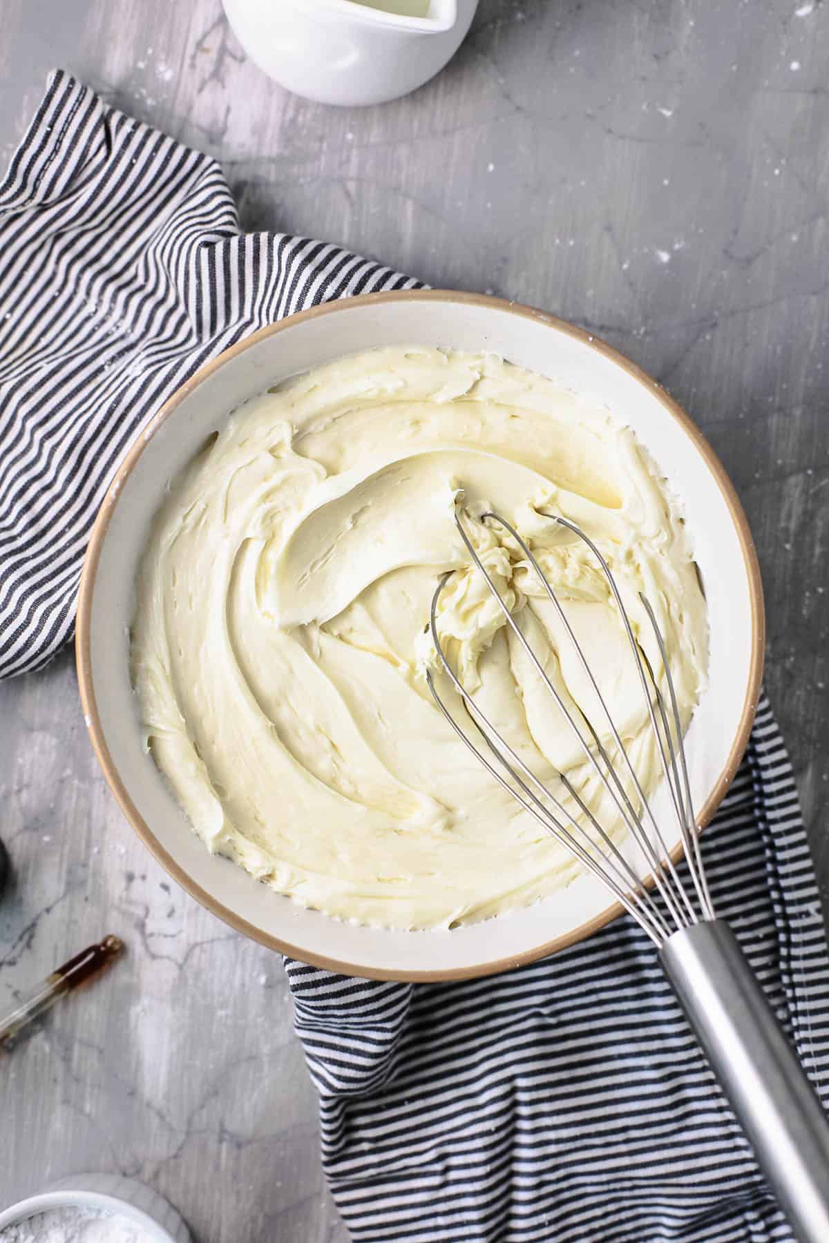 A bowl of buttercream on a counter with whisk in it.
