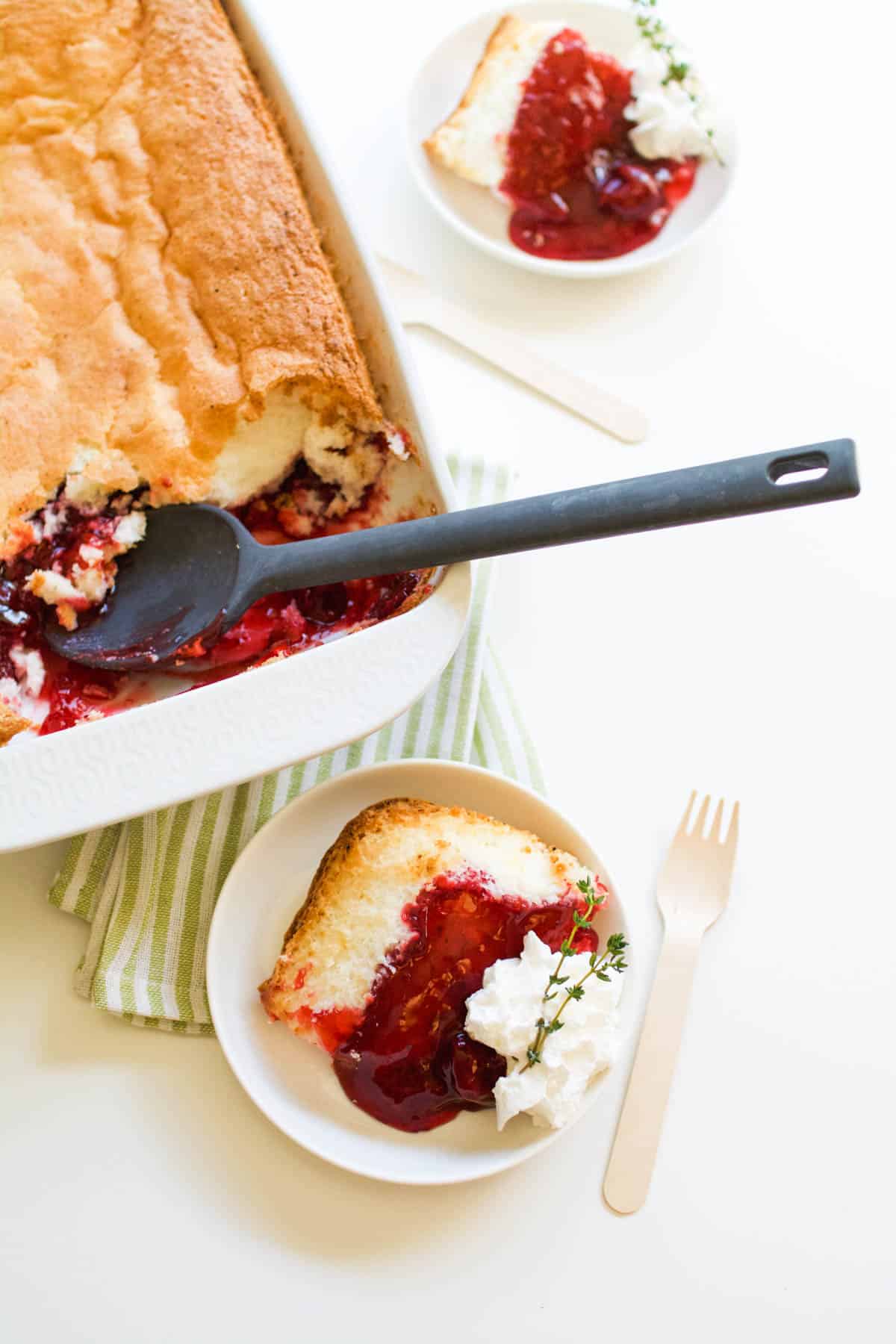 An overhead view of a strawberry shortcake dump cake next to two dessert plates with servings on them.