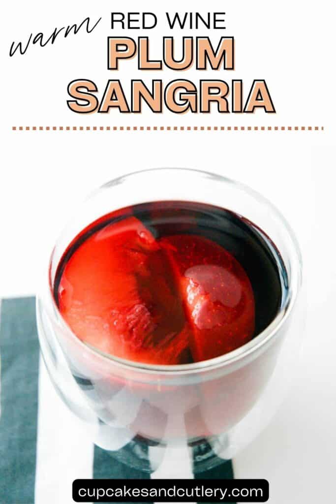 Text: Warm Red Wine Plum Sangria with a glass of red wine sangria on a table with slices of plum.