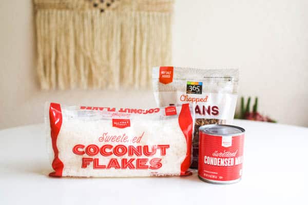 A bag of coconut, a bag of pecans and a can of condensed milk on a table to be used as a topping for a dump cake.