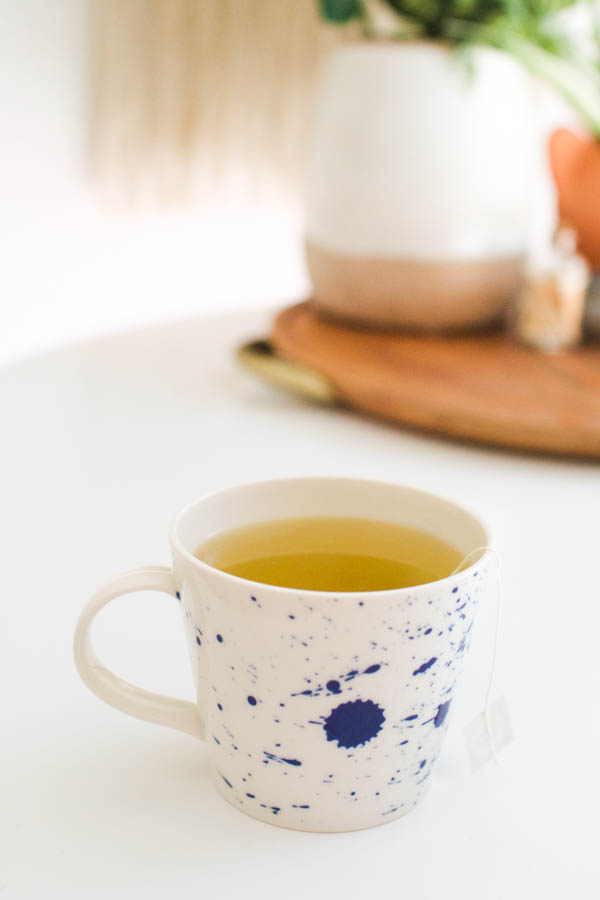 Green Tea Hot Toddy with Vodka on a side table in a white mug with blue paint splashes.