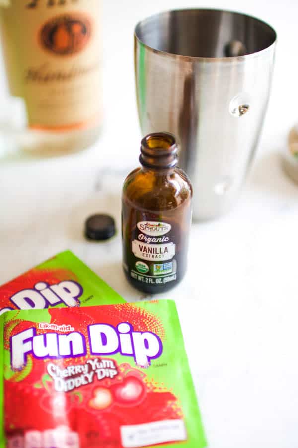 A bottle of vanilla on a counter next to a cocktail shaker. 