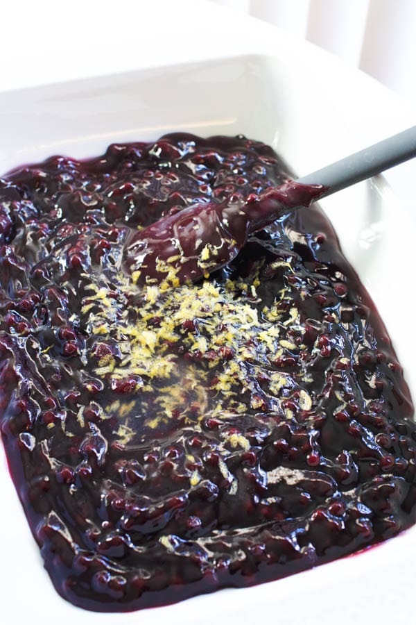 blueberry pie filling in a baking dish with lemon zest for a dump cake.