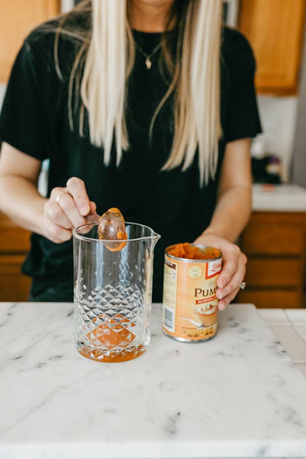 Woman adding canned pumpkin to a cocktail jar.