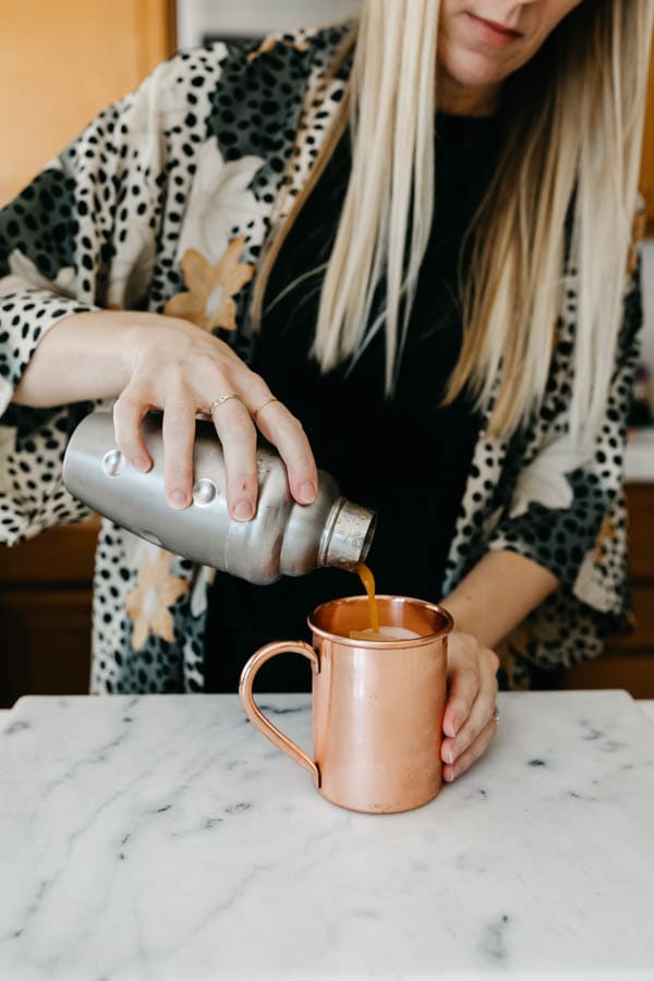 Pouring a pumpkin spice moscow mule into a copper mug.