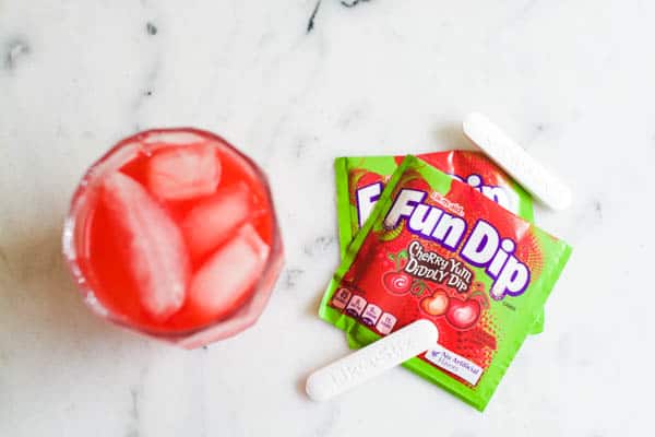 Overhead shot of a cocktail on a table next to a pouch of Fun Dip candy. 