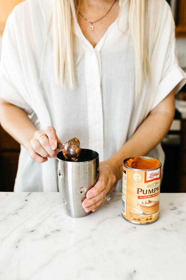 Woman adding pumpkin to a cocktail shaker.