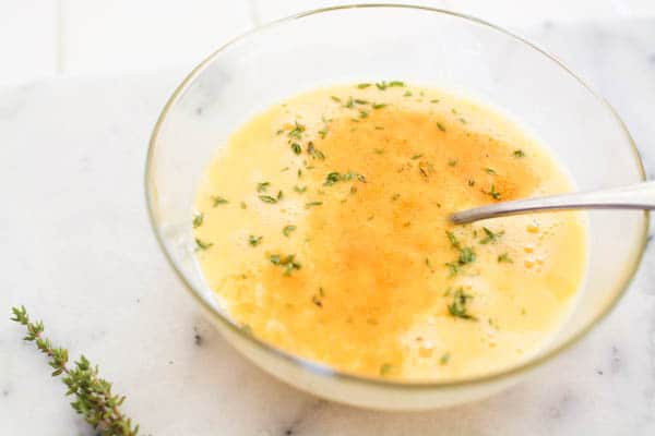 eggs in a bowl with seasoning and thyme reading to be made into a vegetarian scramble